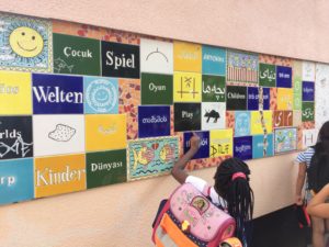 Kultur macht stark-Projekt 2019: 3 Kinder vor Wandtafeln mit den Worten Kinder, Welten und Spiel in verschiedenen Sprachen